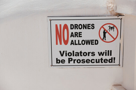 Iron signboard with inscription in English "No drons are allowed. Violators will be Prosecuted!" in beige stone wall. Using drones is prohibited in this area.