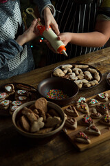 Children decorate homemade gingerbread cookies with cream and sugar topping. Flat lay