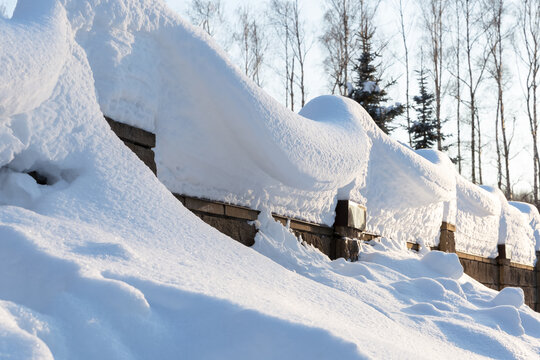 Overhanging beautifully curved snow caps on a fence in sunlight.Soft focus. Snowy winter concept.