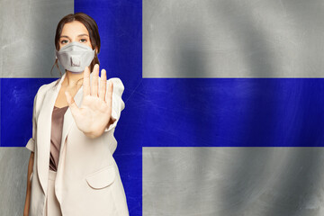 Woman in protective medical mask showing stop gesture on flag of Finland background