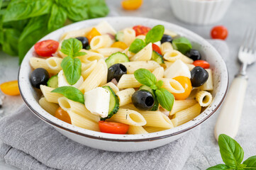 Healthy pasta salad with tomatoes, cucumbers, red onions, olives and cheese in a bowl on a gray background. Copy space.