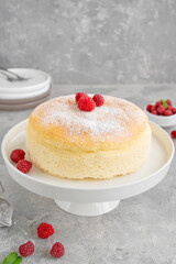 Japanese cotton cheesecake on a stand on a gray concrete background with fresh raspberries and powdered sugar on top. Selective focus, copy space.