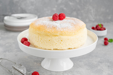 Japanese cotton cheesecake on a stand on a gray concrete background with fresh raspberries and...