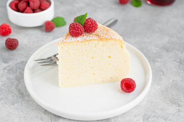 Japanese cotton cheesecake on a stand on a gray concrete background with fresh raspberries and powdered sugar on top. Selective focus, copy space.