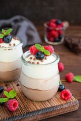 Dessert three chocolate in a glass jar with fresh blueberries, raspberries and blackberries on top on a dark wooden background. Dessert with three layers of different taste. Copy space.