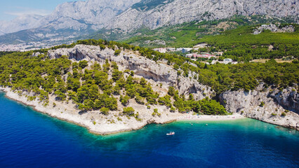 This is a beautiful coastal beach in Makarska, Croatia. The turquoise waters embrace the sun-kissed sand and the powerful waves crashing against the shore offer a peaceful escape from the busy world. - obrazy, fototapety, plakaty