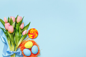 Easter eggs in a nest candy bouquet of pink tulips on a blue background. Flat lay copy space top view.
