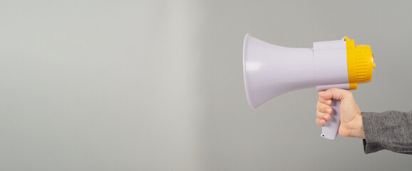 A hand is holding megaphone and  wearing a dark grey T-shirt on grey background.