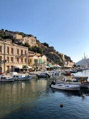 Fototapeta na wymiar Symi island town centre and Aegean sea view. One of small Greek Dodecanese islands. Small marina with boats and yachts. Aegean Sea and island view. Turquoise blue water colourful buildings small boats