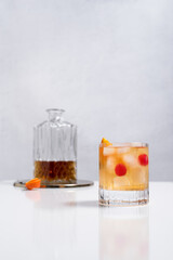 Vaso de vermut rojo con hielo decorado con una rodaja de naranja y cereza sobre mesa blanca