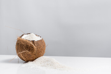 Coco abierto con hojuelas de coco ralladas que se derraman sobre una mesa blanca	