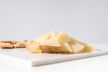 Trozos de queso manchego de oveja curado con tostadas de pan crujiente sobre una mesa blanca. Tapas españolas