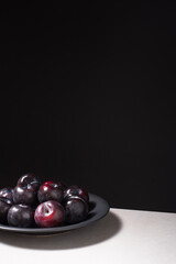 Ciruelas negras maduras en un plato negro sobre fondo negro	