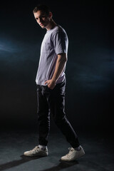 Handsome young man wearing a gray t-shirt and black pants poses on black background in a studio