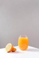 Un vaso de zumo de naranja exprimido en un vaso de cristal con trozos de naranja sobre una mesa blanca con un fondo gris	