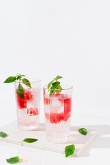 Dos vasos de zumo de sandía con hojas verdes trozos de sandia y hielo sobre fondo claro	
