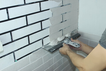 Close-up of a builder's hand applying putty through a stencil. Home repair, decorative plaster in the form of a brick on the wall. Make a brick white wall at home in the interior