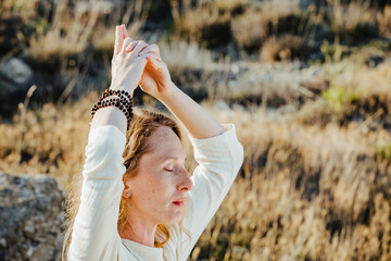 A young woman with closed eyes performs their yoga exercises on the background of rocks in the sun
