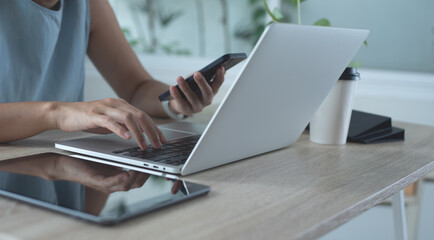 Asian business woman working on laptop computer and using mobile phone surfing the internet in...