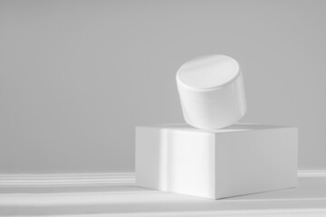 Levitating white jar of cream on square stand in rays of sunlight. White isolated background with shadows. Concept of 3d podium for demonstration of beauty products, mockup, corporate identity