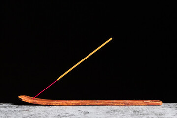 A stick of incense stands on a wooden stand isolated on a black background