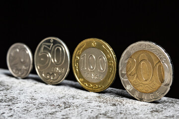 Kazakh coins in denominations of 20, 50, 100 and 200 tenge stand on a table on a black background