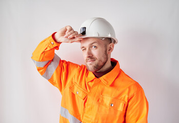 Cheerful looking at camera young caucasian engineer, worker, supervisor or building contractor in white helmet and orange jacket correcting his hardhat. Building industry concept. High quality image