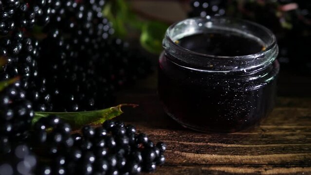 Close-up fresh red juice in a glass jar, black elderberry on a wooden table, homeopathy herbal treatment