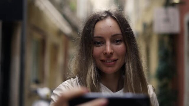 Blonde woman in old city taking photos on modern smartphone, making self portraits