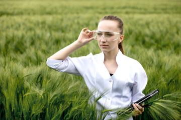 Young woman farmer wearing white bathrobe is checking harvest progress on a tablet at the green...