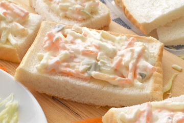 Creamy coleslaw sandwich on a bamboo cutting board. 