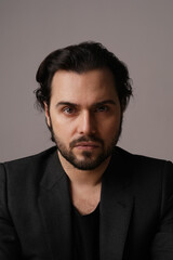 Headshot of bearded man in suit sitting over white wall looking at the camera.