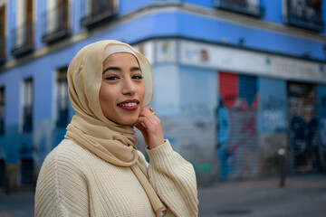 Portrait of cheerful muslim woman wearing a hijab isolated with blue background. Horizontal view of...