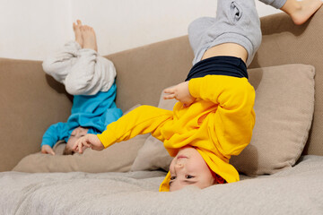 Obraz premium Two little caucasian kids doing gymnastic handstand exercise in living room. Children standing on hands upside down and having fun together. Sport at home. Workout in the apartment. Healthy lifestyle.