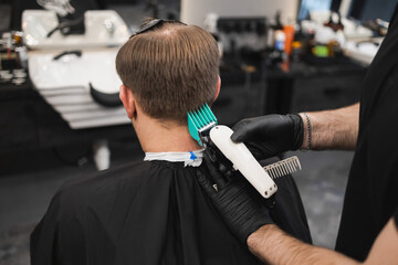 Man getting hair cut at the barbershop. Male barber cutting hair on client's head with clipper