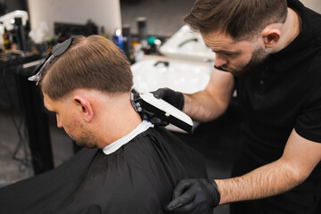 Young man in barbershop. Hairdresser cuts the hair from the back of the client's head with a electric clipper