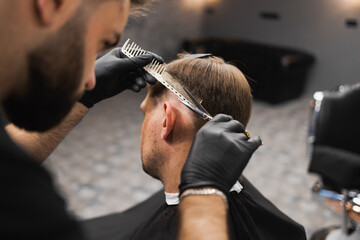 Hairdresser scissors hair on the head sides for a stylish black-haired man in the barbershop