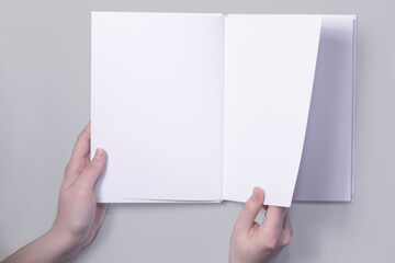 mockup of an open book with a hand turning the page. Applicable for design presentation