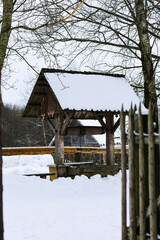 Old wooden well in the village. Winter Russian landscape. An wooden hut, a log house with a thatched roof. Abandoned Russian village covered in snow.