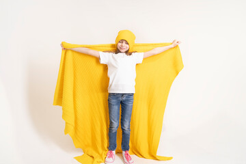 A 7-8-year-old girl in a yellow hat, white T-shirt and jeans holds a yellow plaid in her hands. The child is playing imaginary heroes.