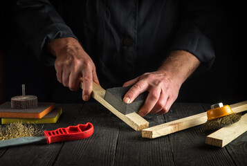 Professional woodworker cleans a wooden planks with an abrasive tools. Hands of the builder close-up during work. Renovation or construction idea