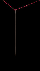 needle hanging on a red thread, isolated on black background, closeup macro