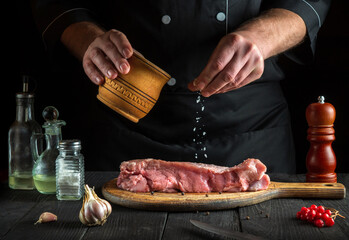 Cook prepares raw veal meat. Before baking, the chef adds salt to the beef. National dish is being prepared in the kitchen