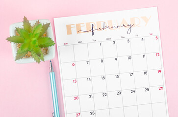 February 2022 calendar and plant pot with pen on pink background.