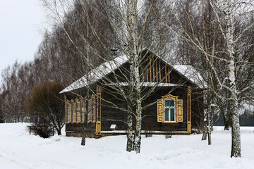 Old wooden house made of gray logs. With beautiful yellow windows and shutters. Winter Russian landscape. Snow covered trees. Abandoned old Russian village covered in snow.