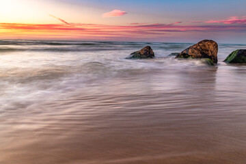 Low angle wide view of the waves crashing on the rocks during sunset at the sea Poleg beach Israel. 
