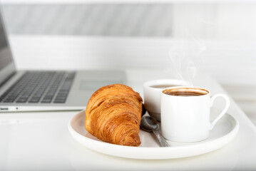 Business lunch with croissant, jam and laptop on a white table.