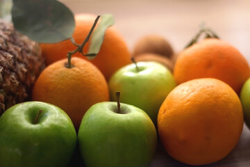 Pineapple, apples, oranges, lemons and kiwis on a wooden table. Selective focus.