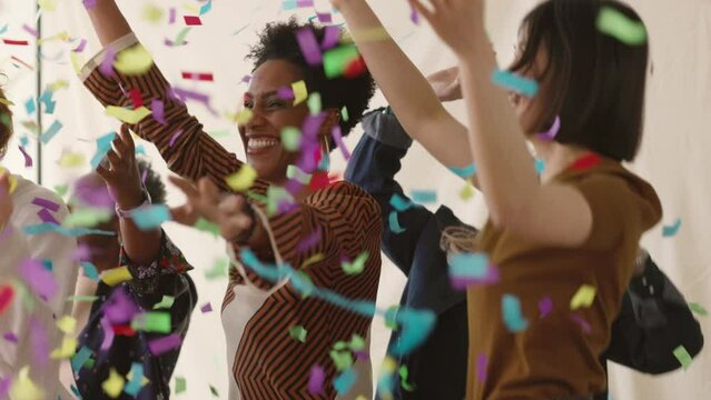 Slow motion of cheerful multi ethnic women celebrating and dancing with confetti falling for International Womens Day