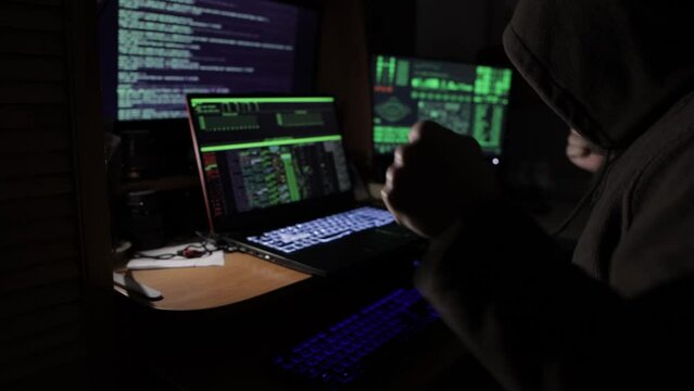 a hacker in a dark room sitting in front of monitors rejoices at the hacking of the security system